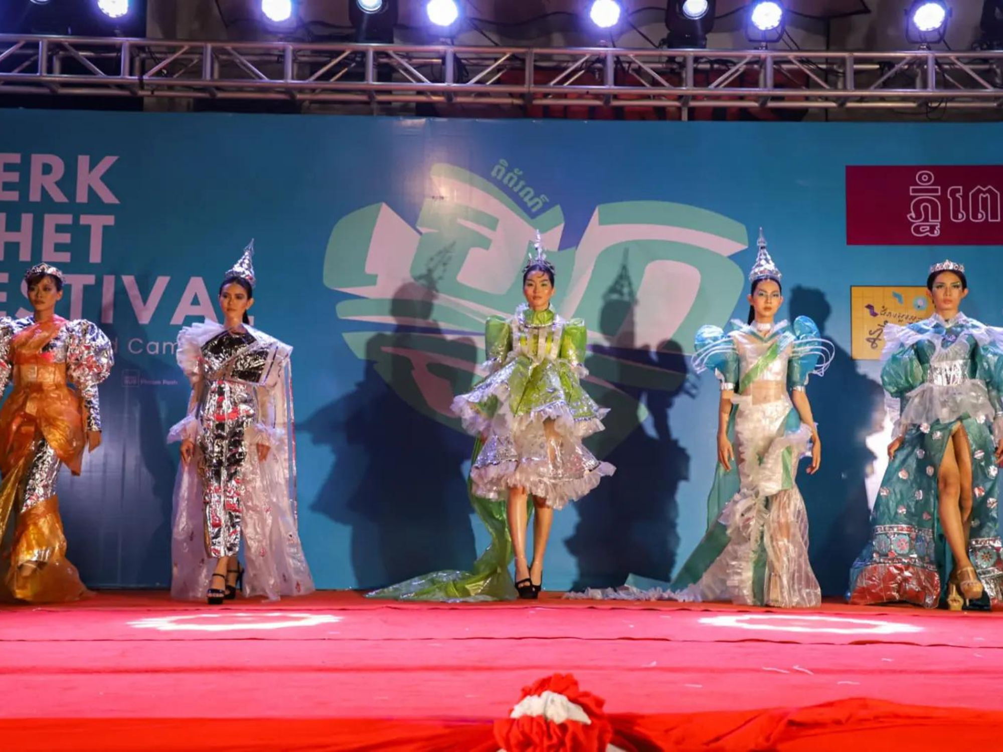 Five people in elaborate outfits walk on a stage as part of a fashion show by La Chhouk at the Berk Chet Festival.