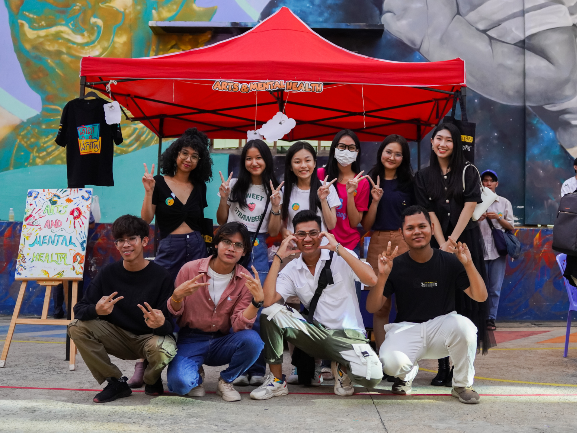 A group of young people pose smiling and laughing for a photo in front of a red tent.