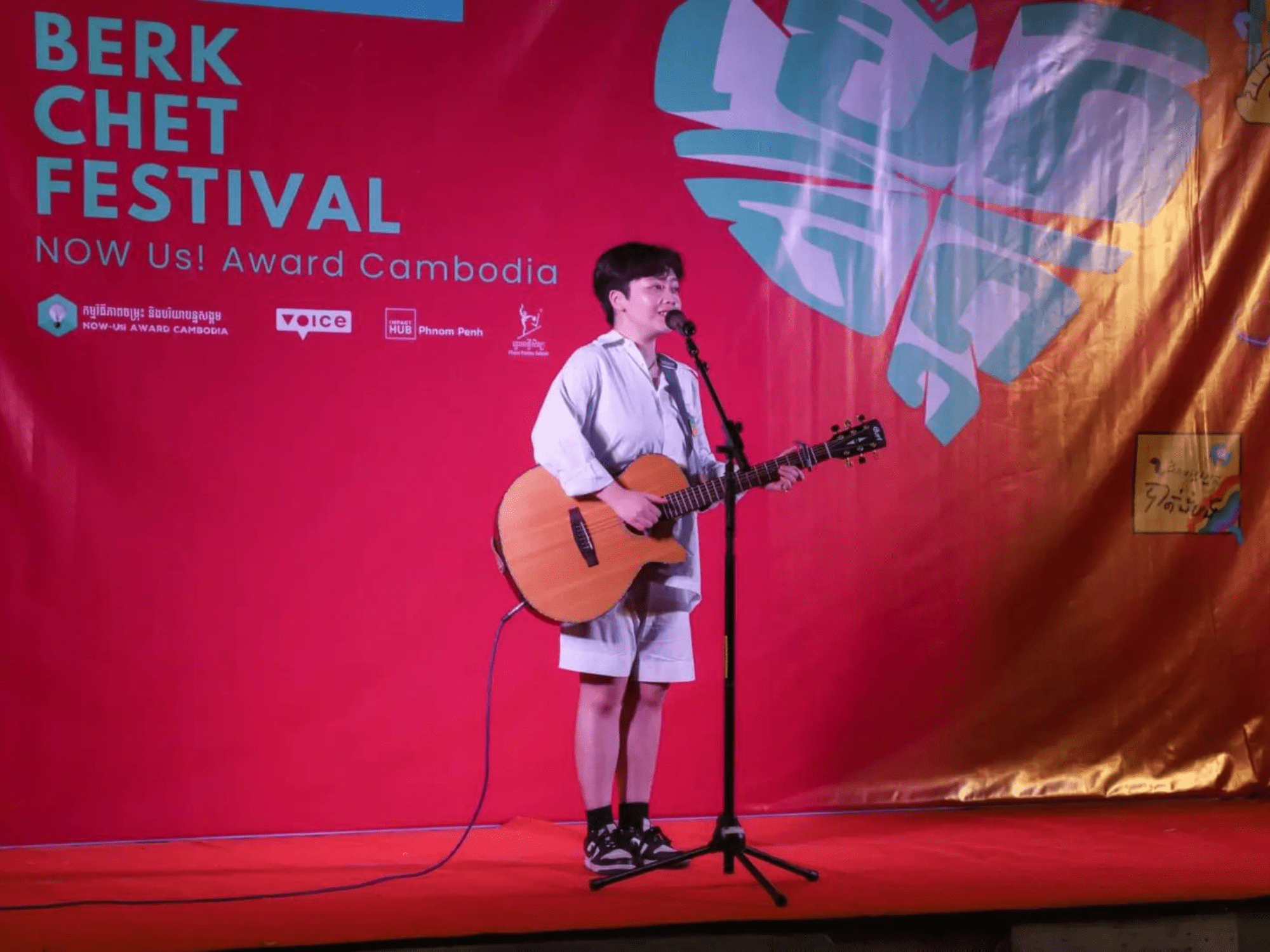 A young person stands on a stage with a guitar singing.