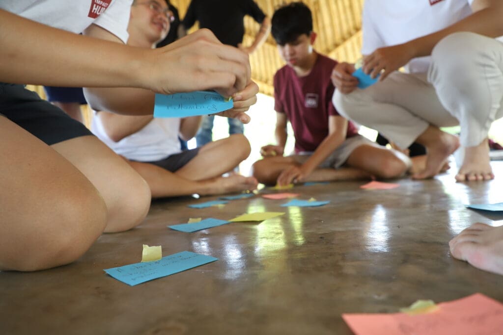 A zoomed in and slightly blurred photo of a group of Impact Hub Phnom Penh staff sitting on the floor and writing on colored paper.