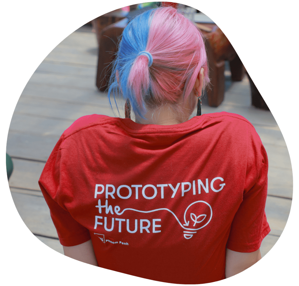 An IHPP staff member seen from the back, wearing a red t-shirt printed with the large words "PROTOTYPING THE FUTURE."