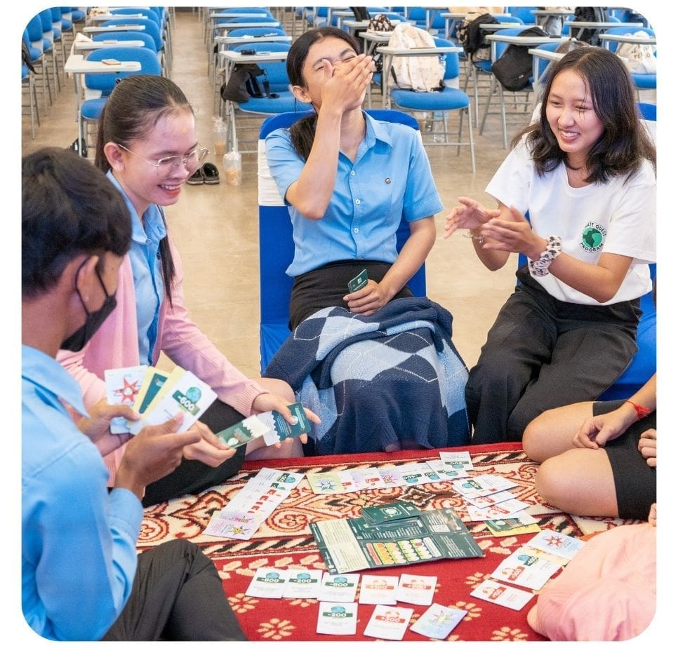 A group of five university students sits on the floor on a rug laughing as they play the Climate Quest card game.