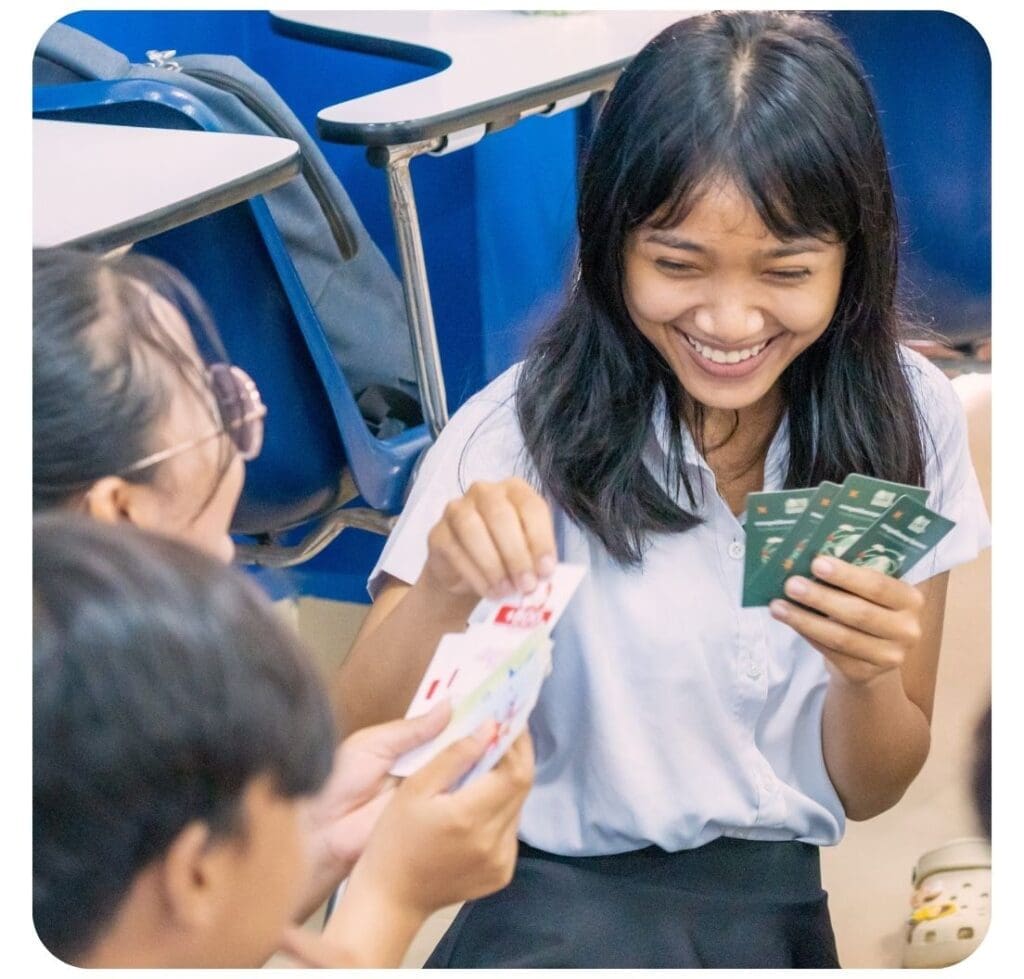 Three university students laugh while playing the Climate Quest Little Earth card game.