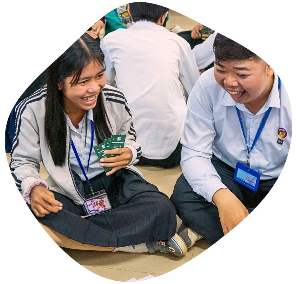 Two youth sit on the floor laughing playing an educational card game about climate change developed by Impact Hub Phnom Penh.