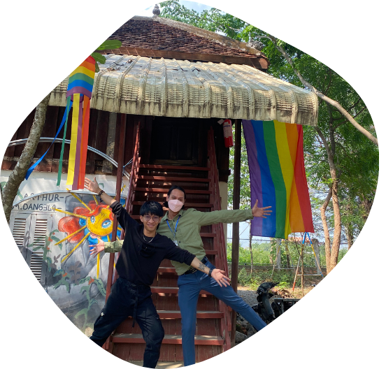 Two young Cambodians stand in front of a house decorated with rainbow pride flags