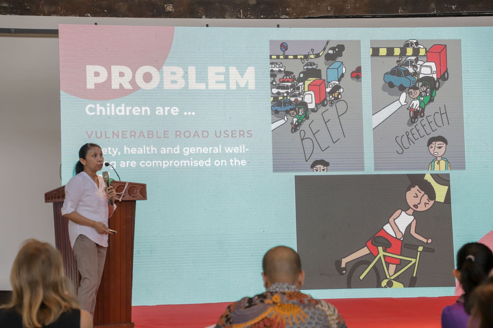 An entrepreneur presents about Multistrands on a stage at the Urban Mobility Incubator with a large powerpoint screen behind her.