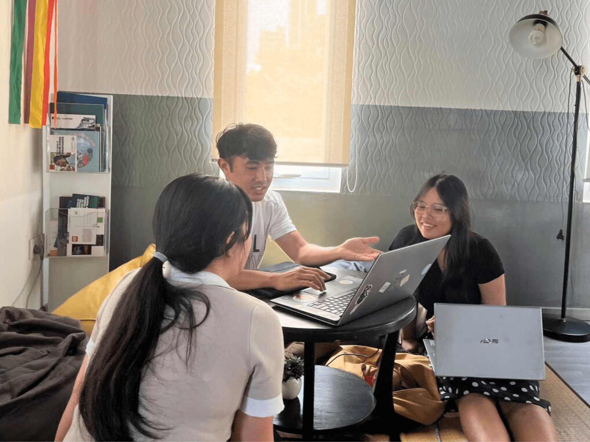 Two content creators in the media4impact accelerator sit around a computer with a team member from Impact Hub Phnom Penh