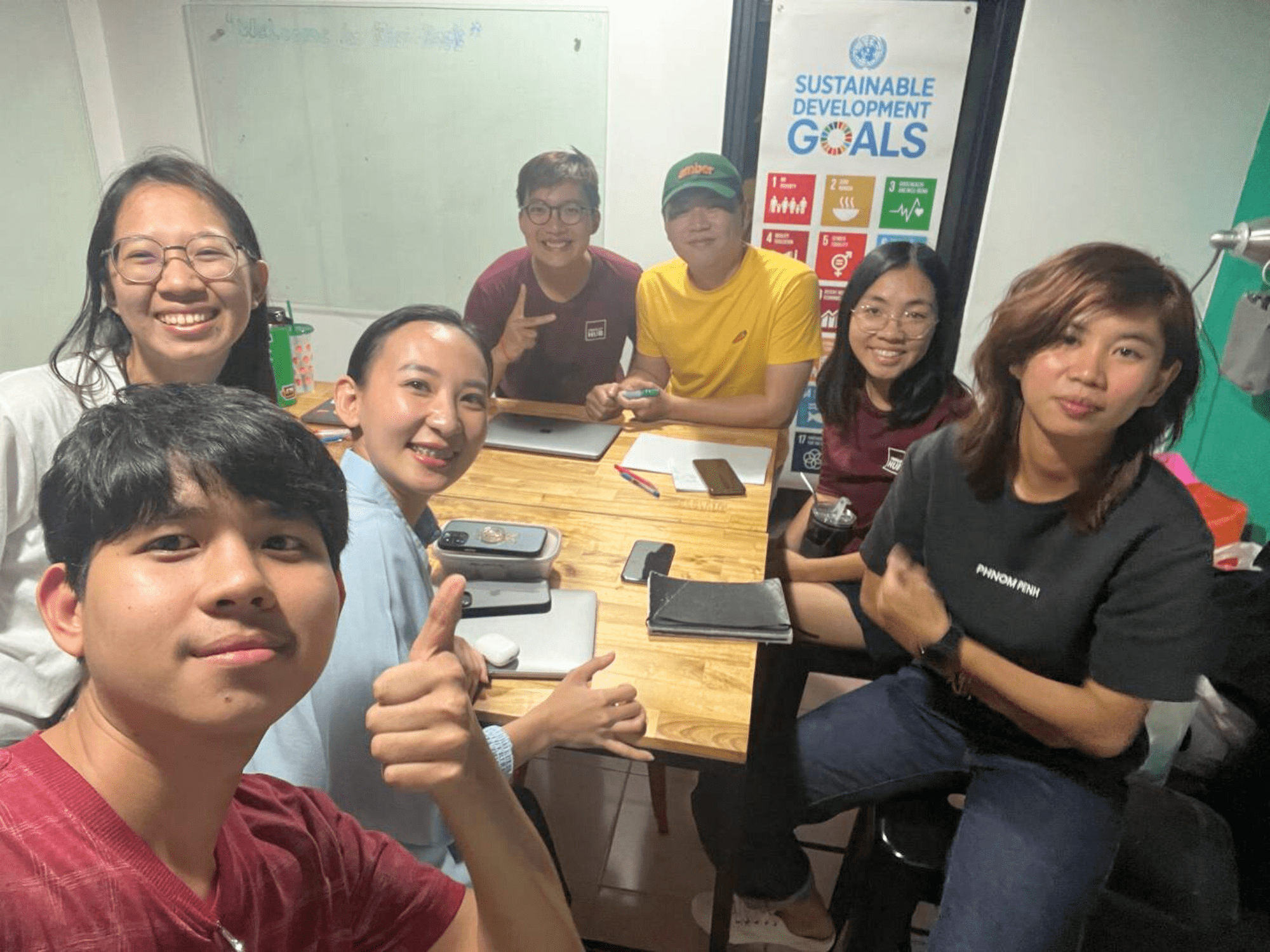 Seven participants and Impact Hub Phnom Penh staff sit around a table during a workshop. They are smiling and posing for the camera.