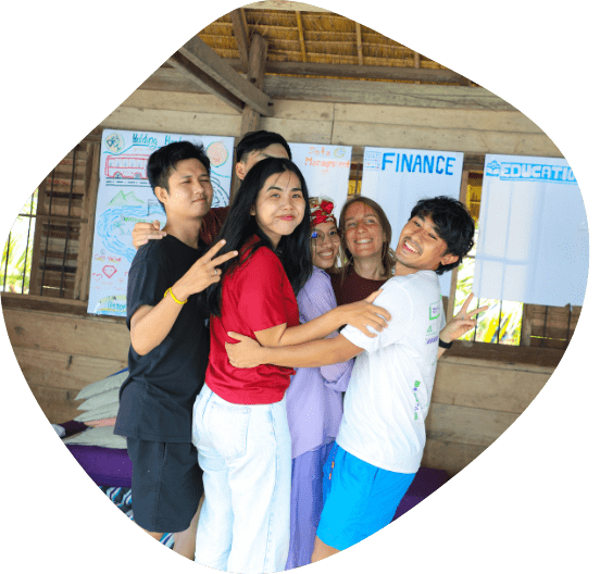 Six Impact Hub Phnom Penh staff in a group hug smile towards the camera during a recent staff retreat. Large flipchart papers with graphics and text are hung up on the wall in the background.