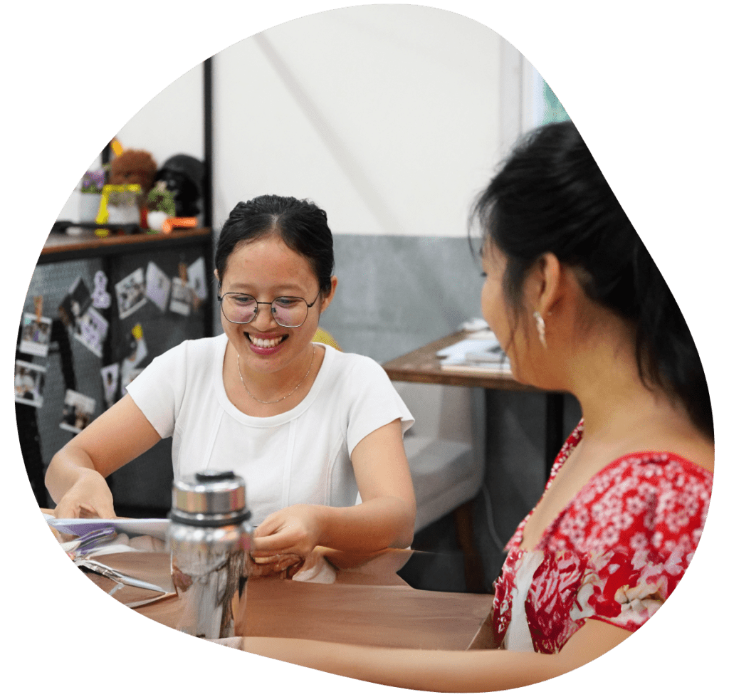 Two young women, including one Cambodian entrepreneur, sit at a table together smiling and talking.