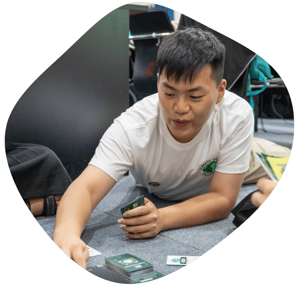 A young man sits on the floor smiling and talking while explaining a card game about climate action made by Impact Hub Phnom Penh through our Climate Quest initiative.