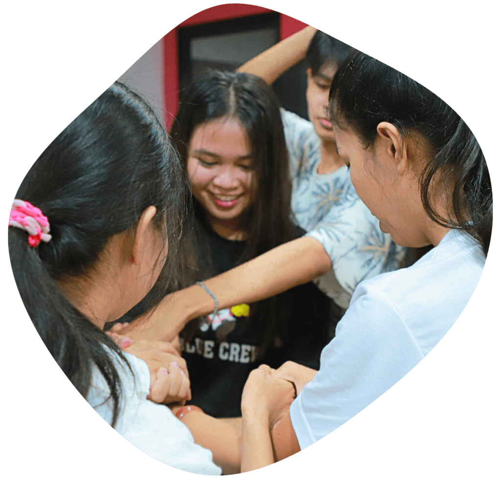 A group of Cambodian youth stand together doing a human knot activity.