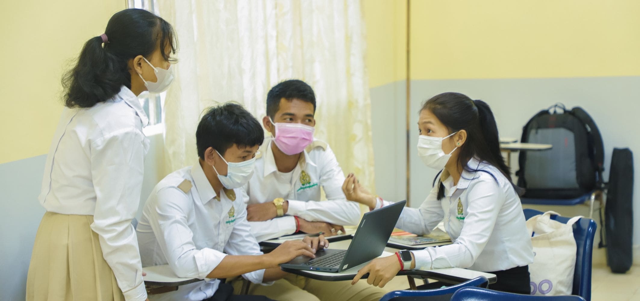 Four Cambodian university students sit around a laptop in a classroom talking during an entrepreneurship class.