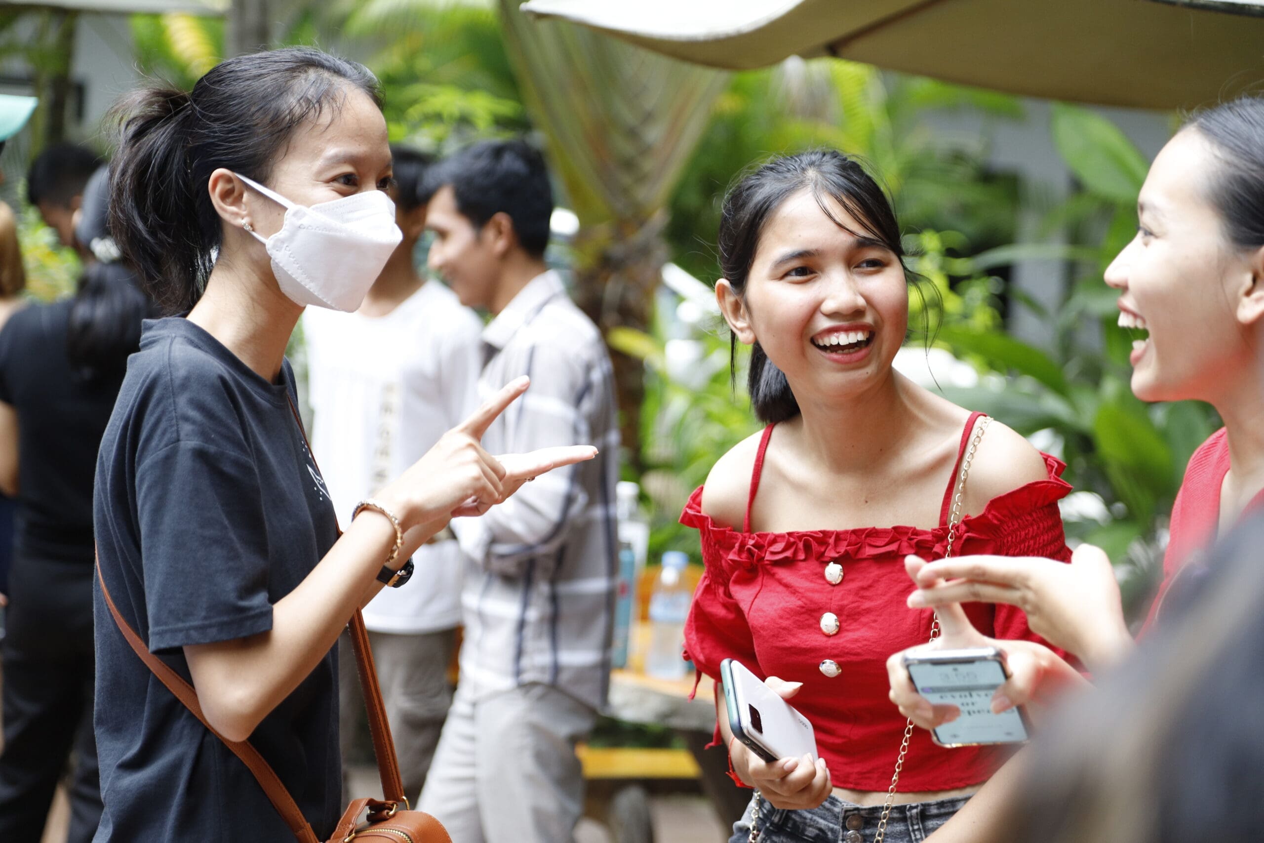 Three young Cambodian women stand talking and laughing.