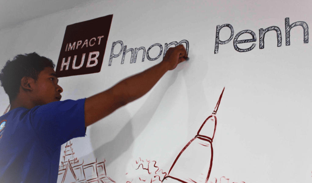 A man draws the Impact Hub Phnom Penh logo on a wall