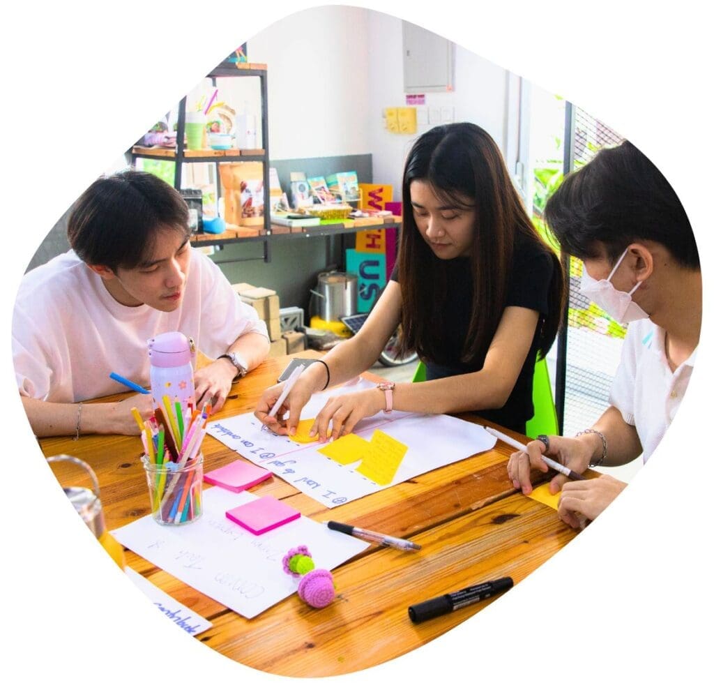 Three young entrepreneurs sit at a table brainstorming with post-it notes at Impact Hub Phnom Penh's office.