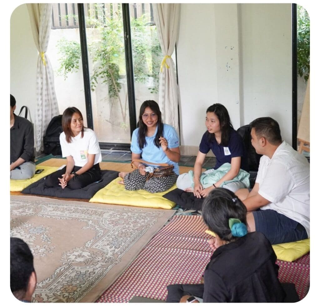 Around five entrepreneurs sit on mats on the ground talking.