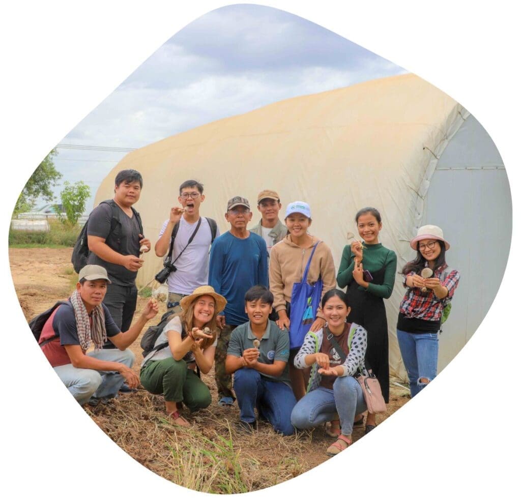 11 entrepreneurs, staff of Impact Hub Phnom Penh, and farmers pose for a group photo in front of a greenhouse in rural Cambodia.