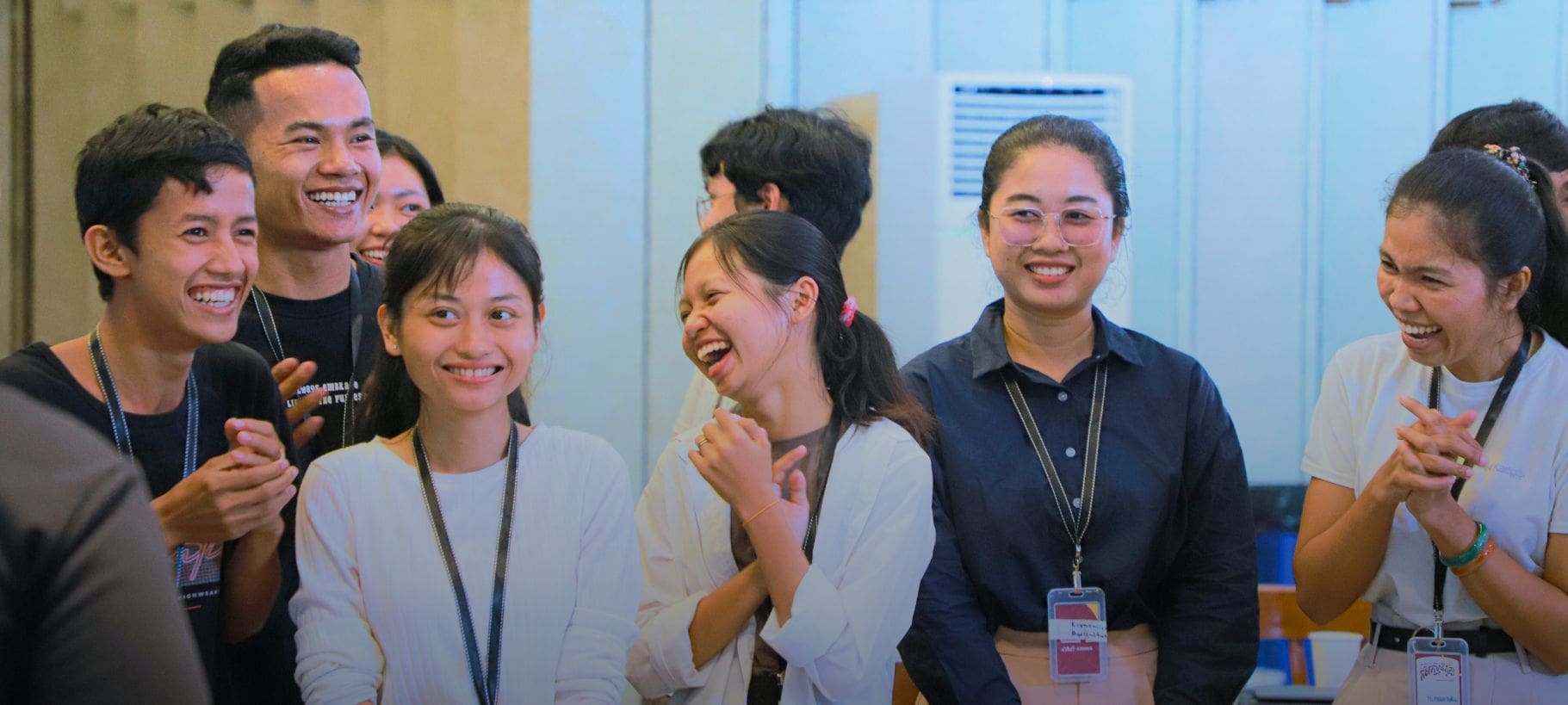 A small group of Cambodian university students stand together laughing and clapping during an Impact Hub Phnom Penh event on sustainable agriculture.