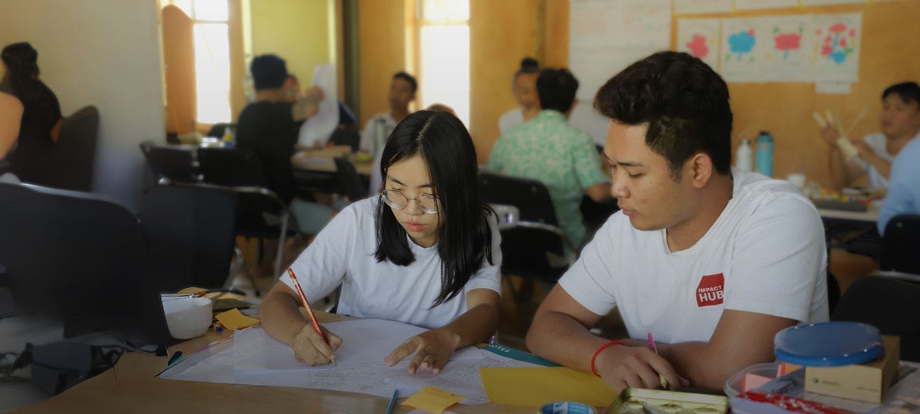 Two young adults sit at a table writing and reviewing a worksheet together.