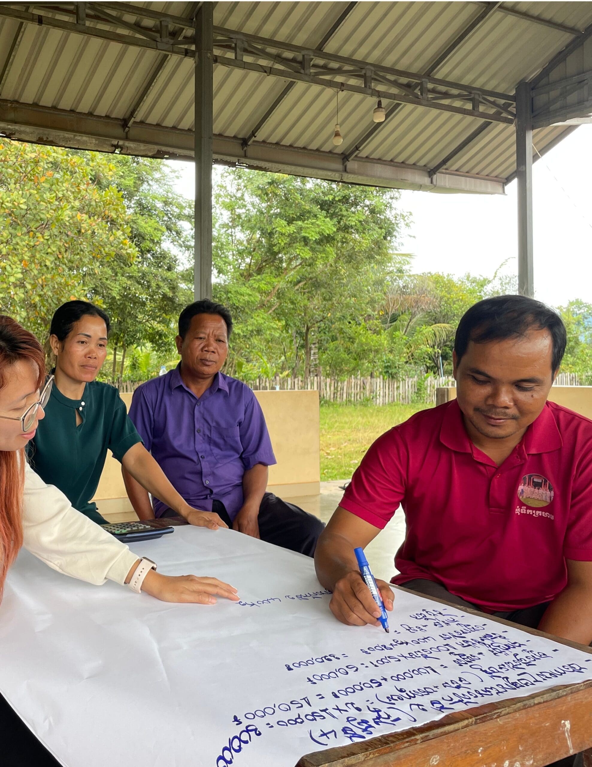 A member of the Tekkrohorm Kelom Or Chivapheab Agricultural Cooperative writes brainstorming ideas on a flip chart with guidance from a mentor.